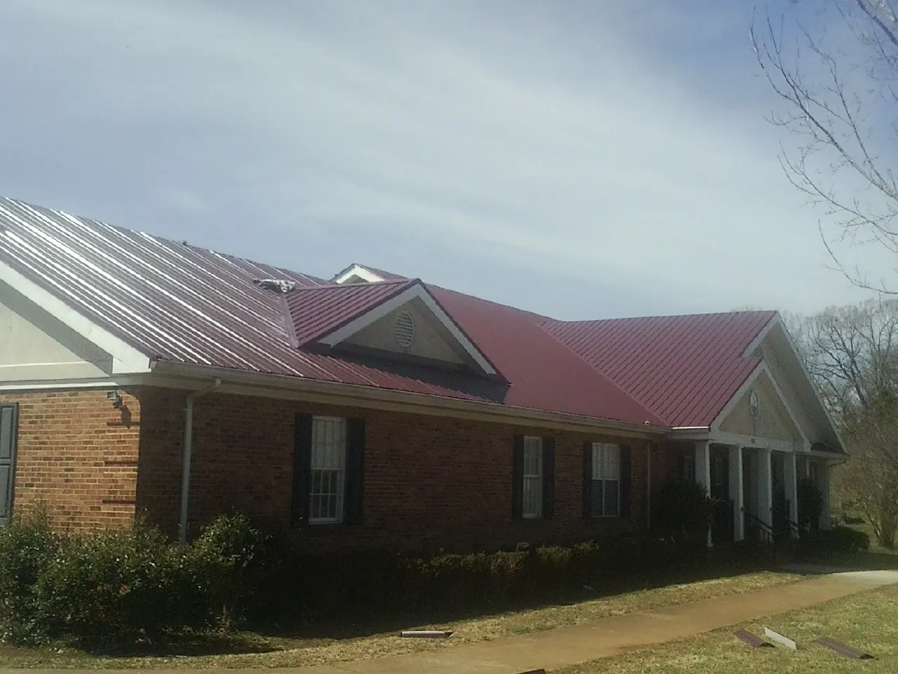 Red metal roof with gabled entries on a long brick building, from a Hail Damage Roof Repair job in Flushing