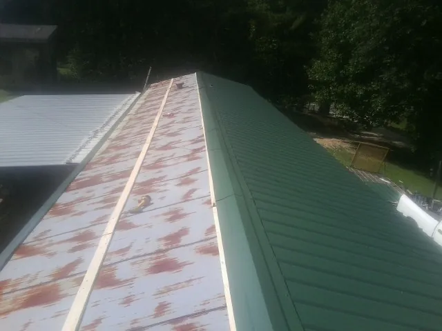 Old rusted panels beside newly installed green metal roofing — Wind Damage Roof Repair by Roofing Brothers in Flushing