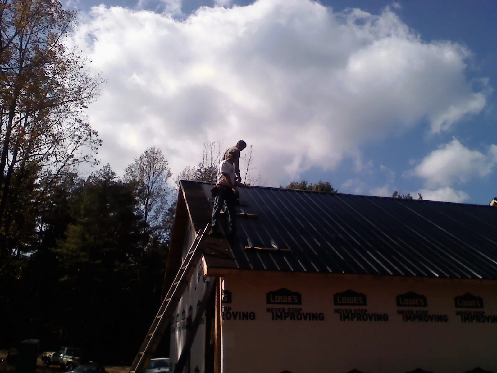 Roofer fastening dark metal panels high against a cloudy sky, from a Roof Inspection job in Flushing