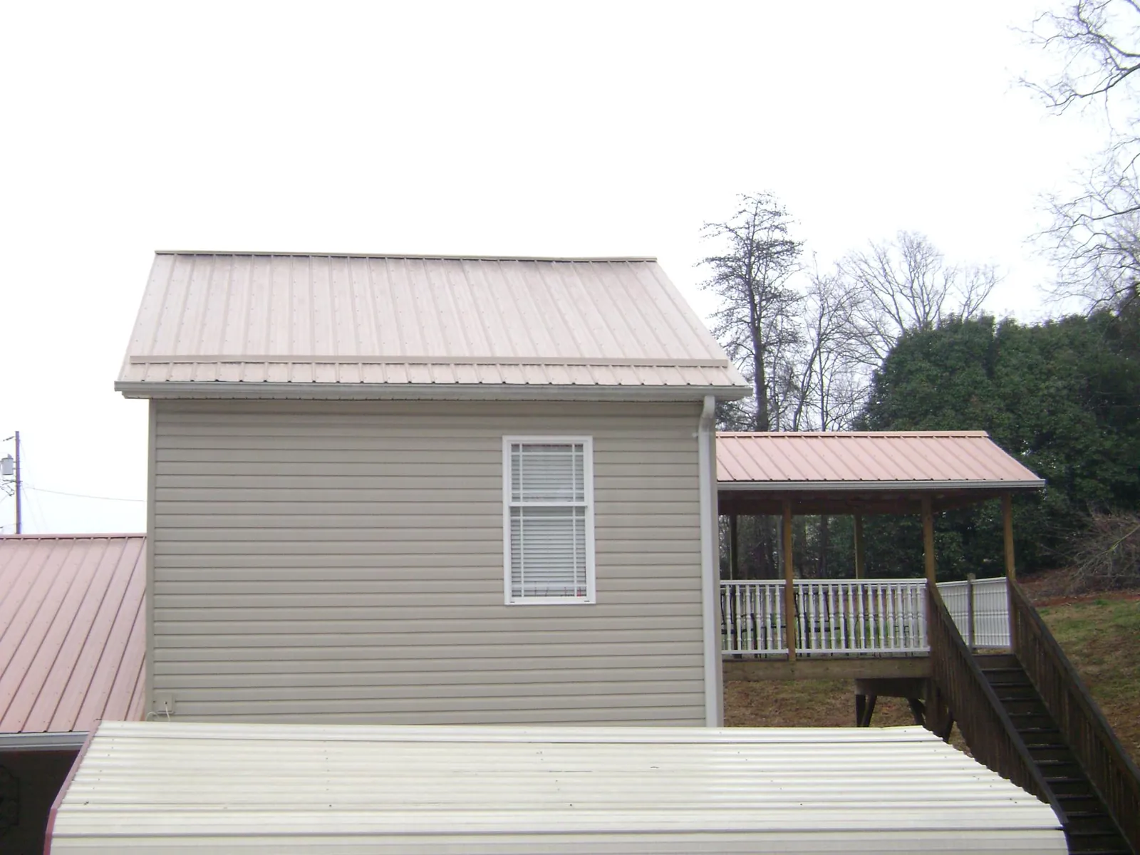 Tan metal roofs on a two story addition and attached porch, from a Roof Replacement job in Flushing